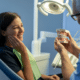 Dentist showing jaw model to a female patient holding her face in pain, discussing TMJ disorders.