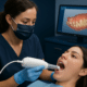 Dentist using an intraoral scanner with a 3D teeth model shown on a monitor.