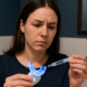 Concerned woman examining an over-the-counter whitening kit with a syringe.